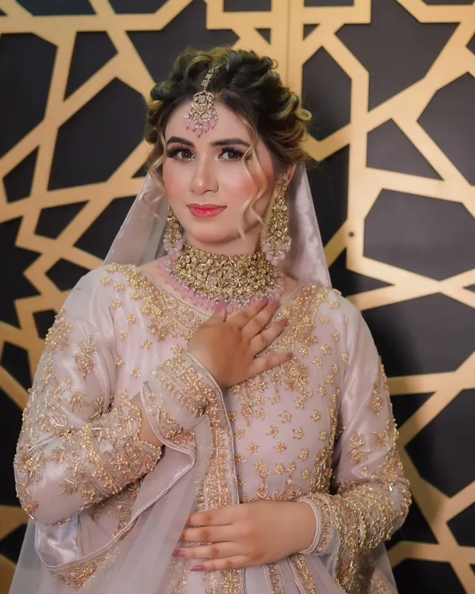 Bride in a blush and gold outfit with traditional jewellery against a geometric gold backdrop