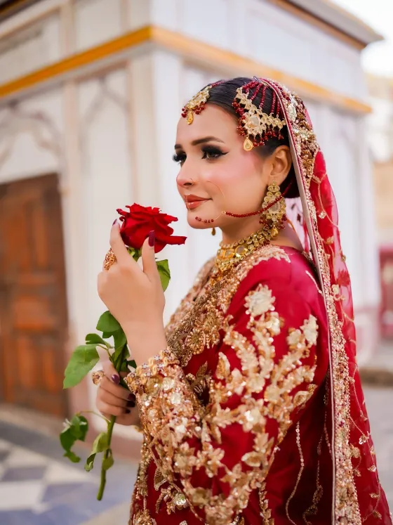 Bride in red and gold holding a rose, makeup by Blush Bar