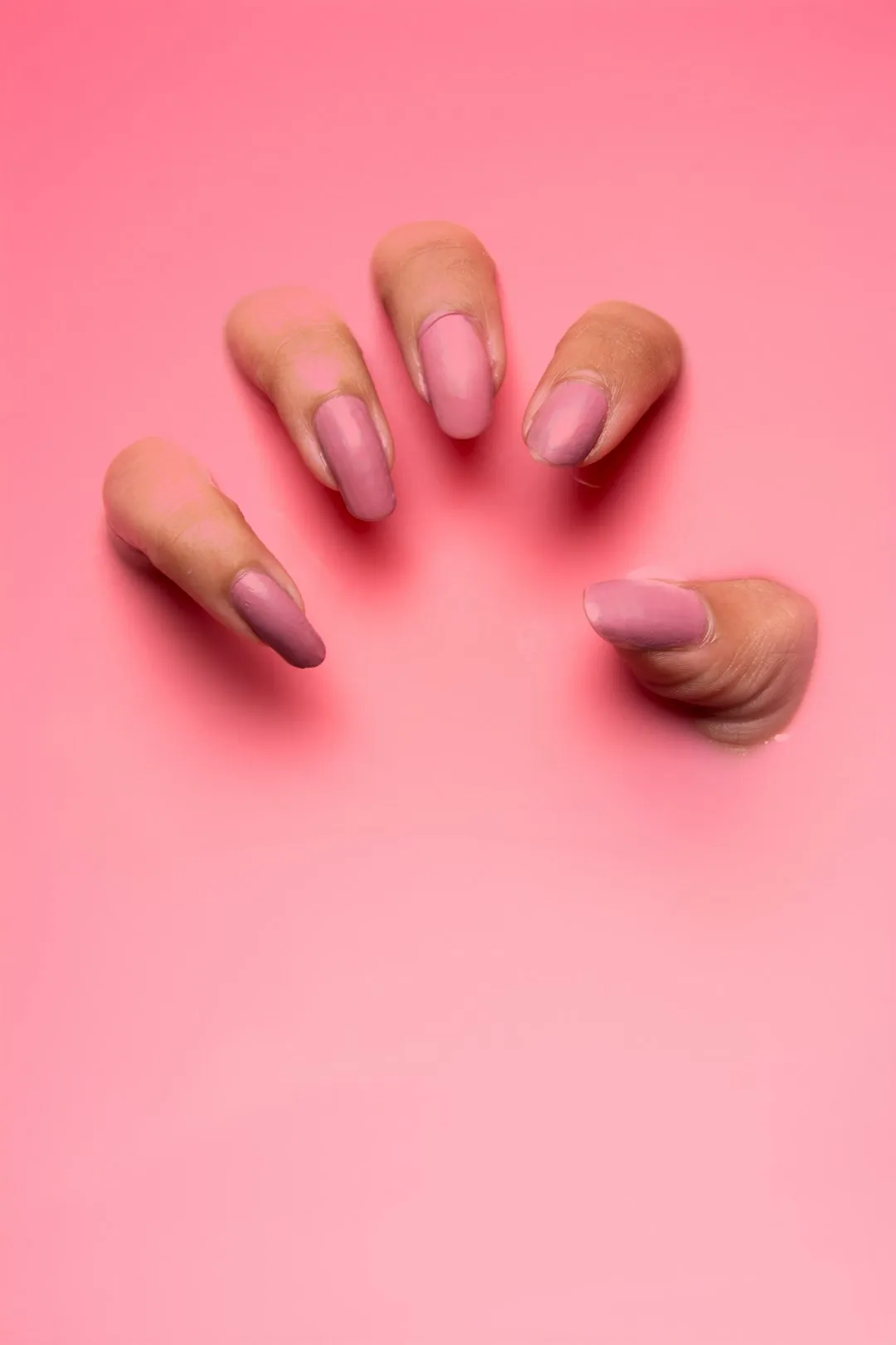 Five fingers painted in pink nail polish emerge from an opaque pink liquid