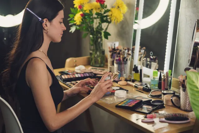 Bride-to-be seated at a mirrored makeup station with palettes and brushes