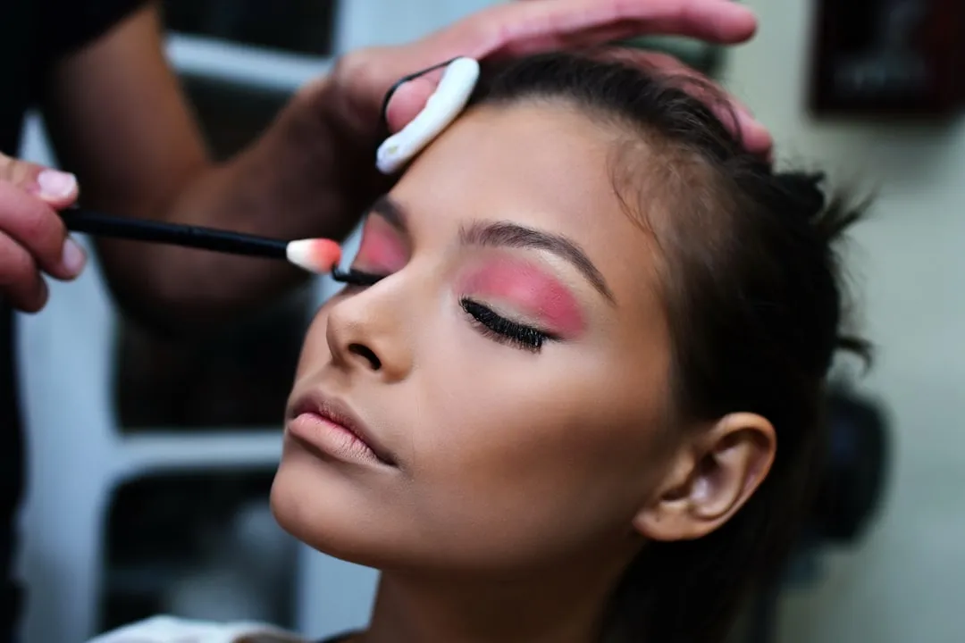Makeup artist blending pink eyeshadow onto a client's closed eyelid