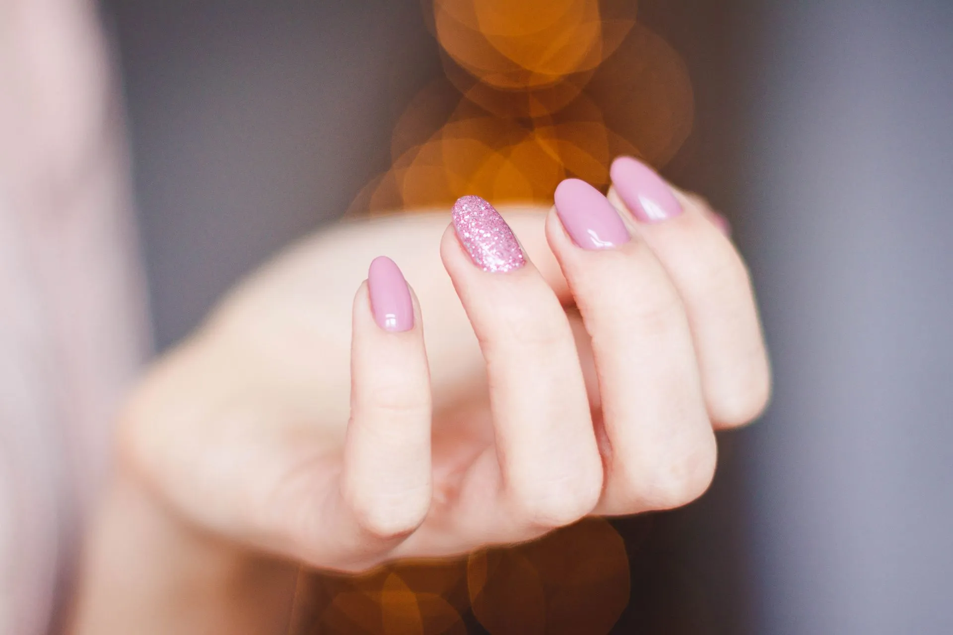 Close-up of a hand with glossy pink gel manicure and one glitter accent nail